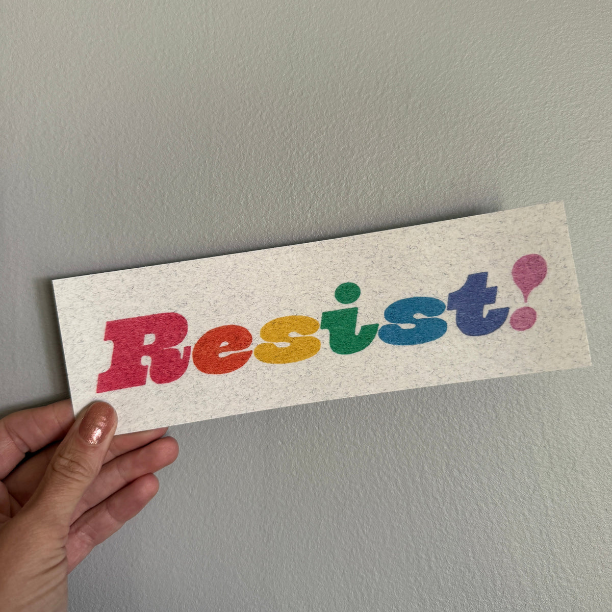 Colorful 'Resist!' sticker on a gray surface with a hand holding it.