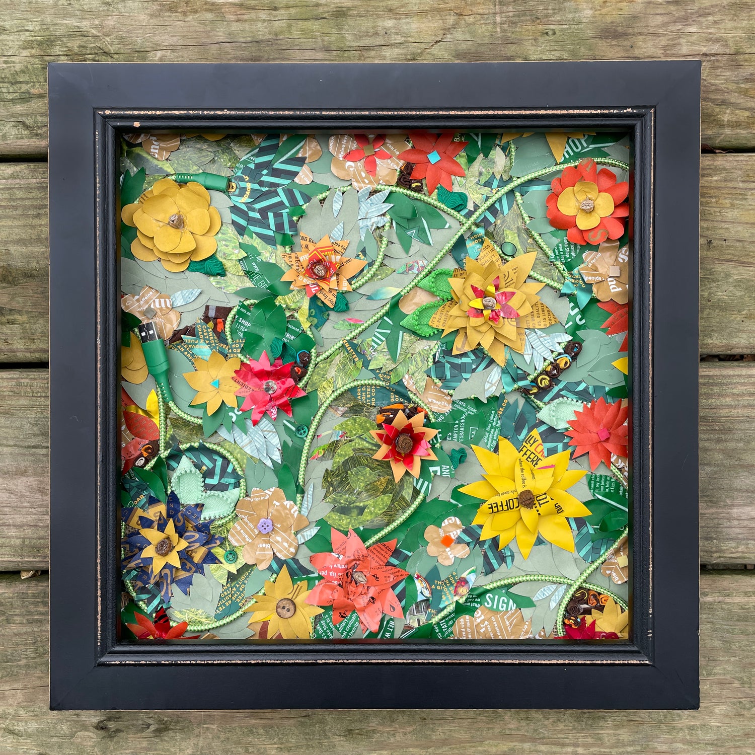 A framed art piece with yellow flowers created from coffee bags on a green background