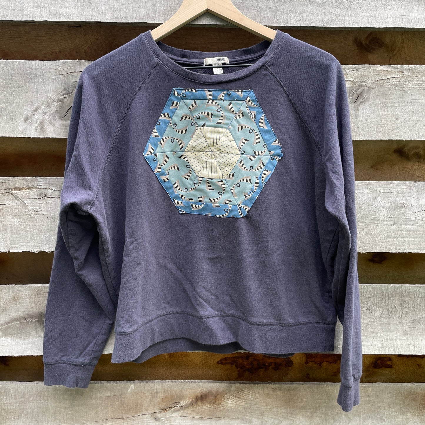 A faded navy blue sweatshirt with a blue hexagonal quilt square appliqué on the front