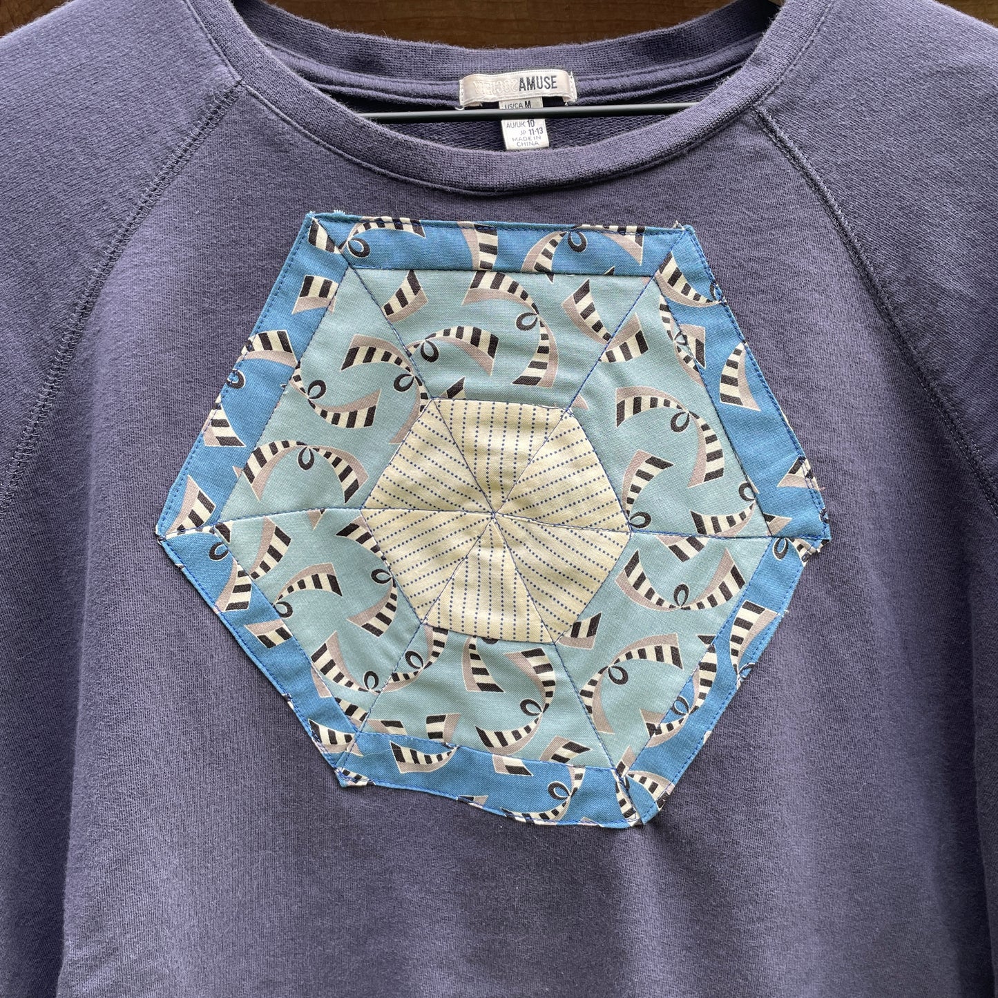 A faded navy blue sweatshirt with a blue hexagonal quilt square appliqué on the front