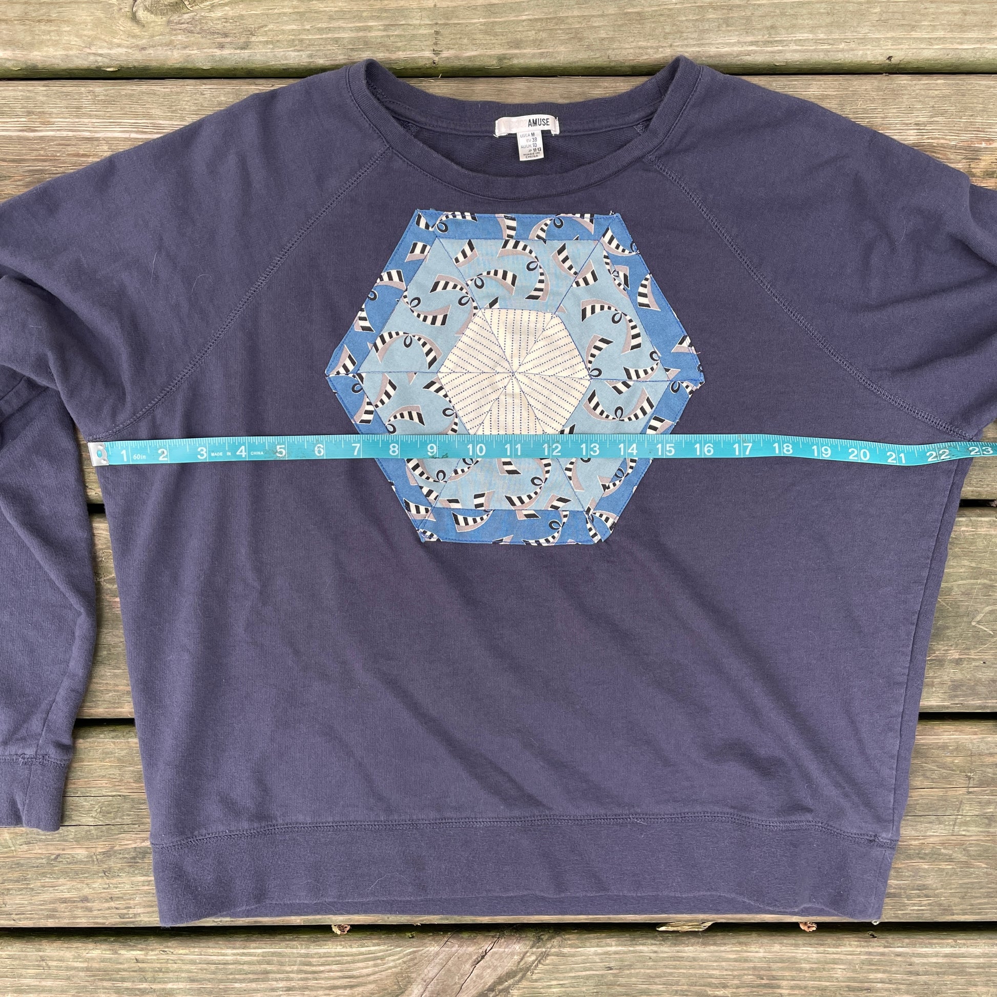 A faded navy blue sweatshirt with a blue hexagonal quilt square appliqué on the front