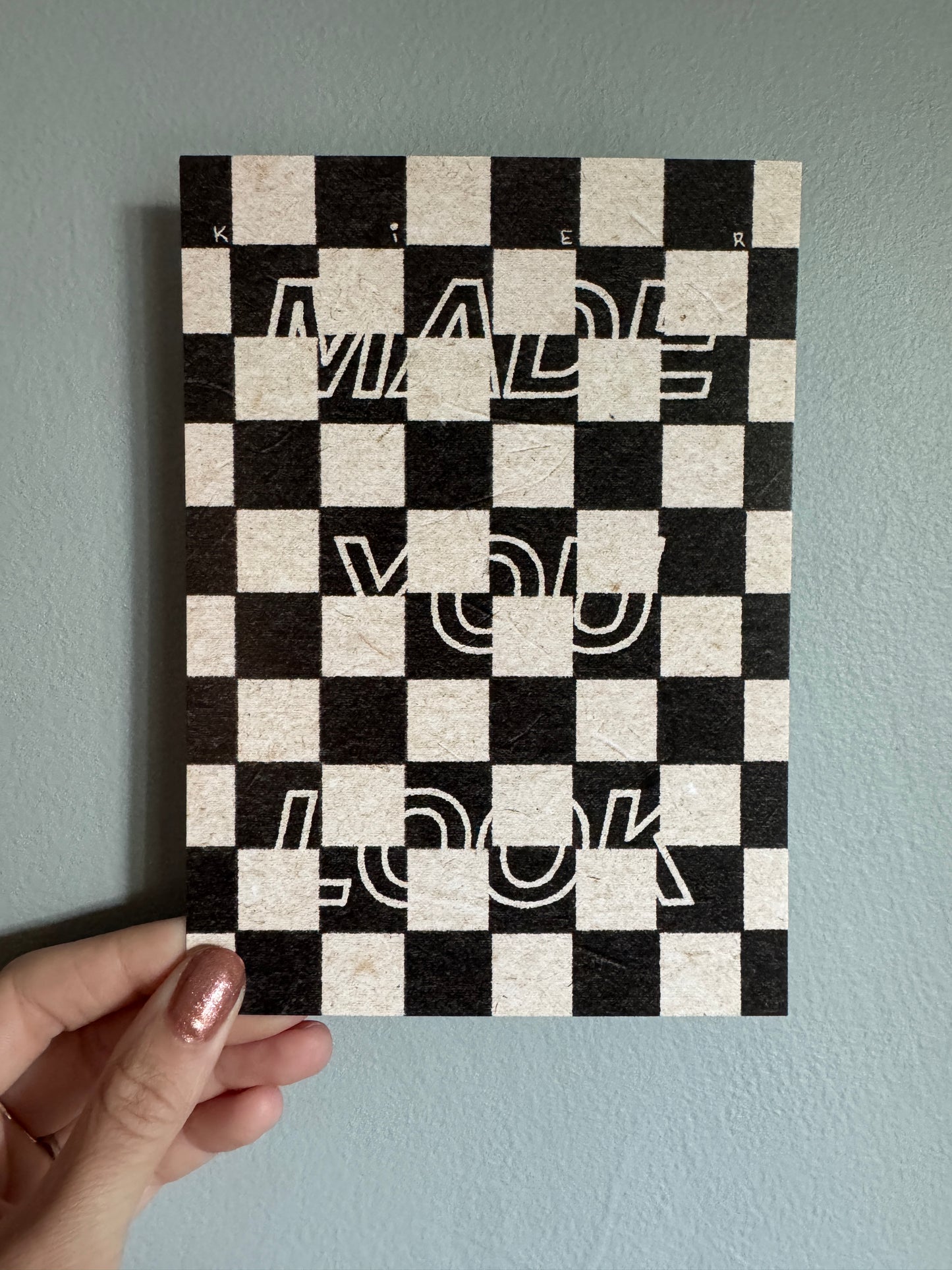 Checkered print with abstract designs held by a hand against a light blue wall