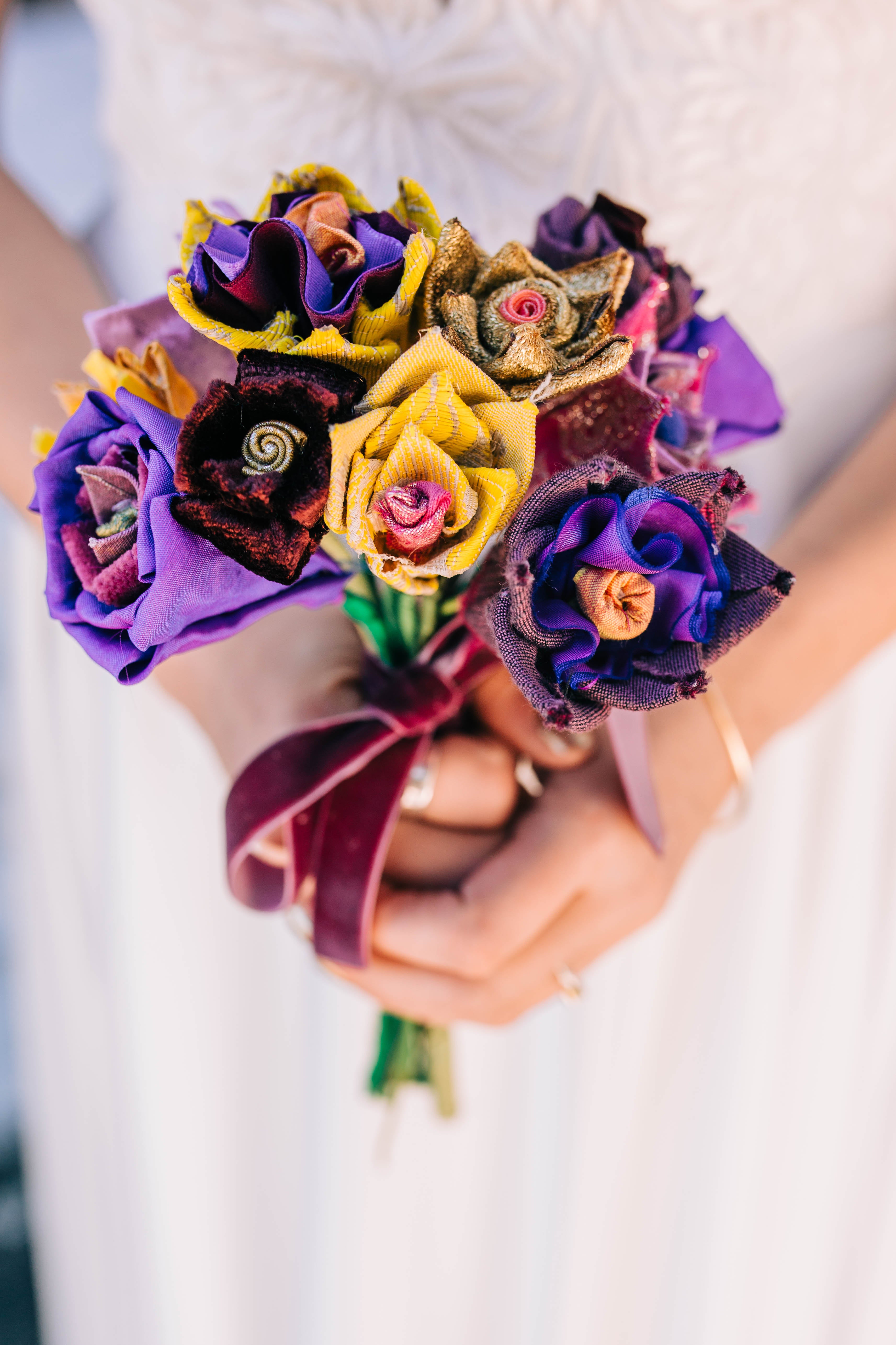 A woman in a white dress holds a bouquet of yellow and purple flowers made from fabric