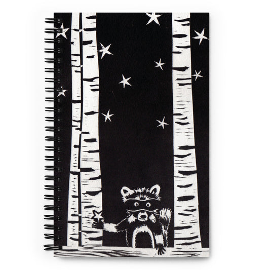 A notebook with a black and white image of a raccoon, trees and stars