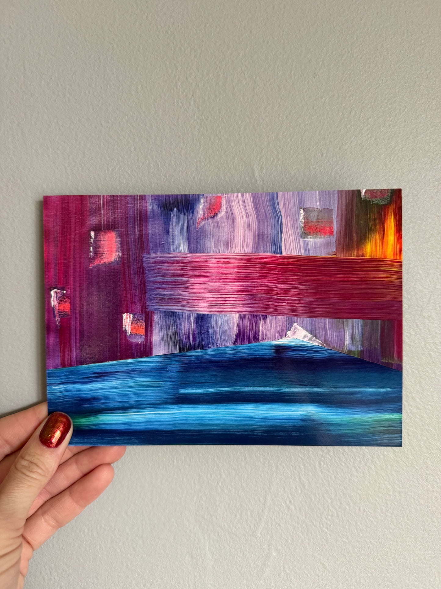 Hand holding a colorful abstract painting against a plain wall