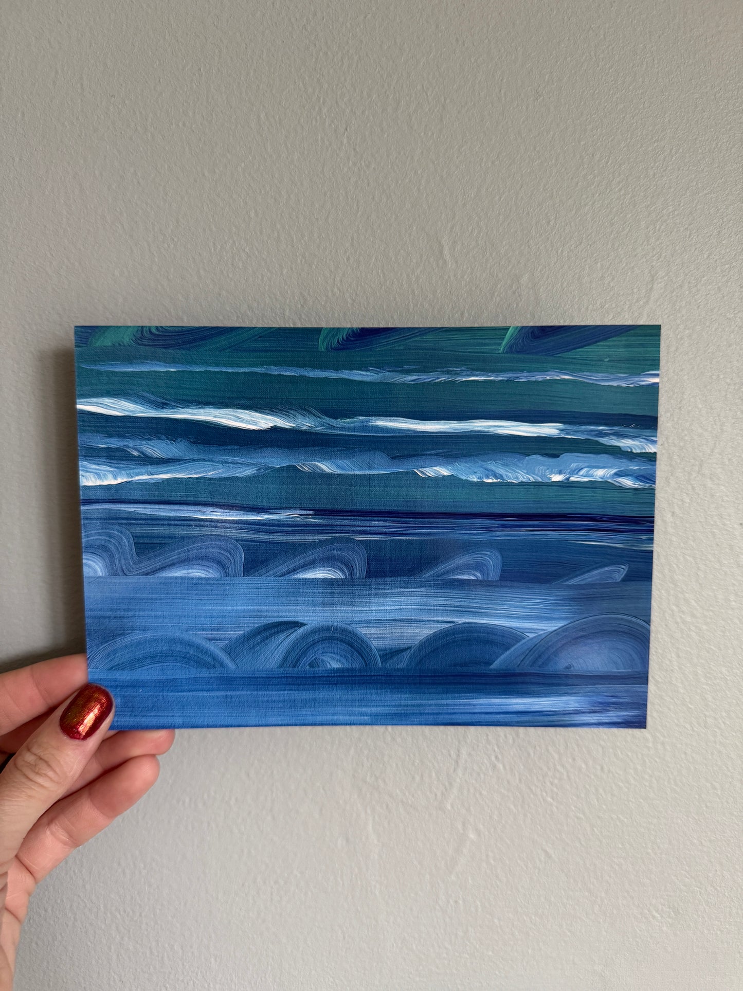 Hand holding a blue abstract painting against a plain wall