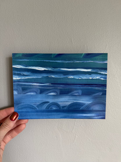 Hand holding a blue abstract painting against a plain wall
