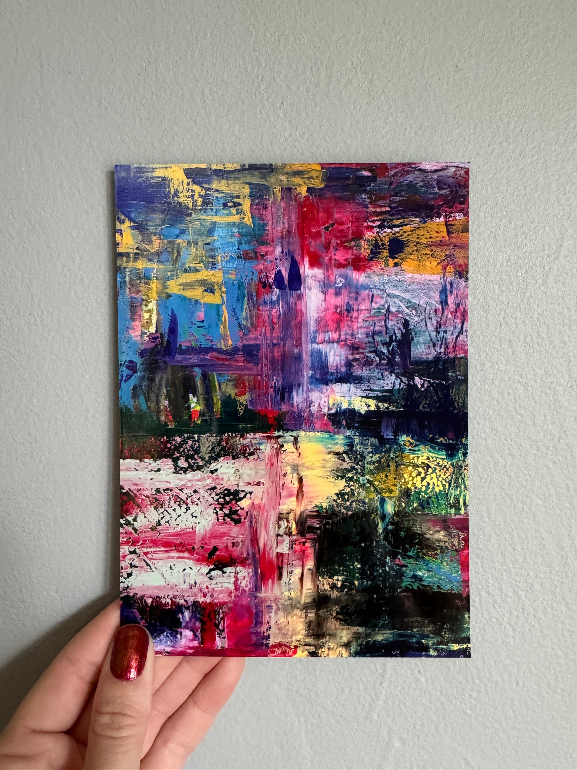 Abstract painting on a postcard held by a hand against a gray wall
