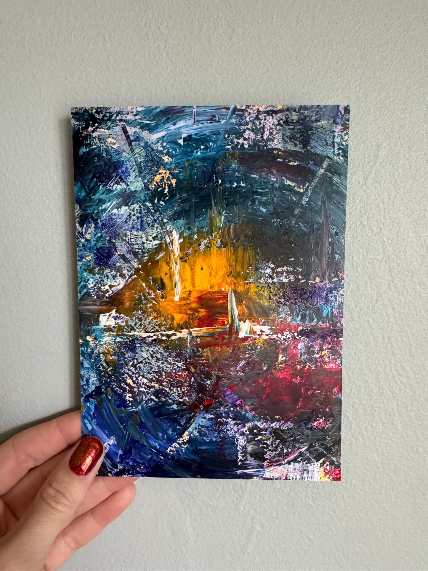 Abstract painting held by a hand against a light gray wall