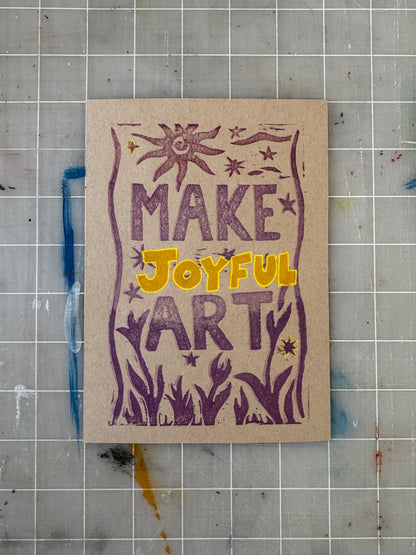 Card with 'MAKE JOYFUL ART' text on a textured surface