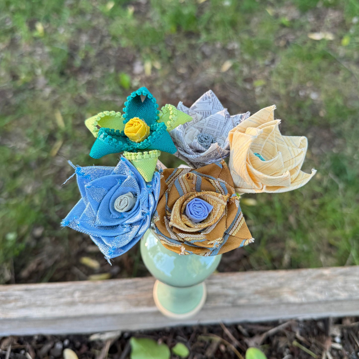 Decorative flower arrangement made of fabric on a wooden plank outdoors.