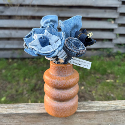 Blue fabric flowers in a brown vase against a blurred natural background