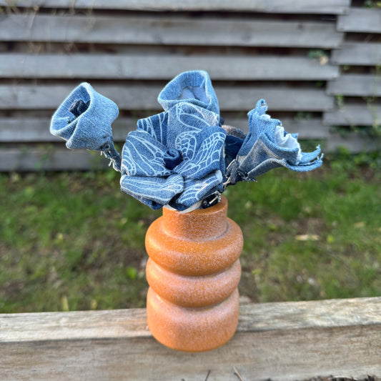 Blue fabric flowers in a brown vase against a blurred natural background