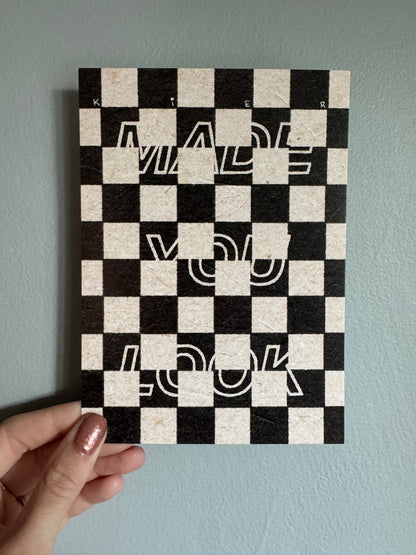 Checkered print with abstract designs held by a hand against a light blue wall