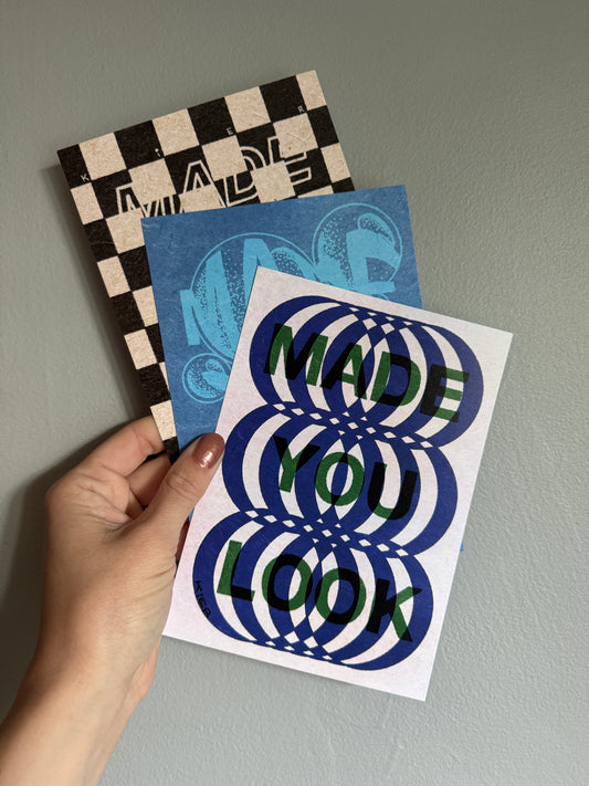 Three artistic postcards with different designs held in front of a gray wall.