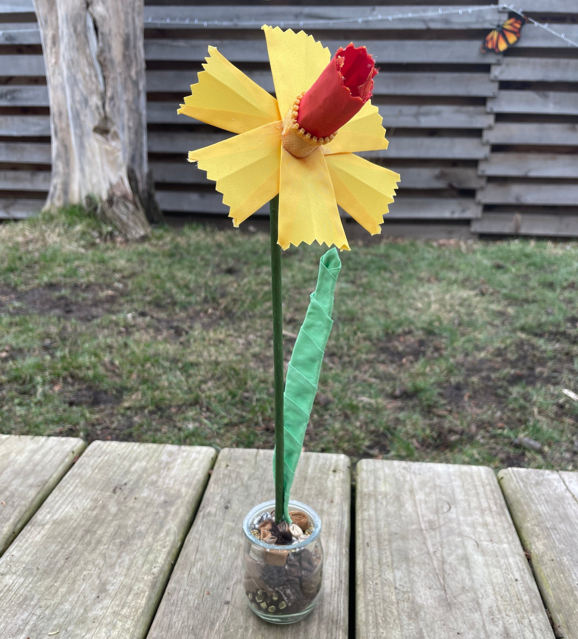 A daffodil made out of yellow ribbon sitting in a jar