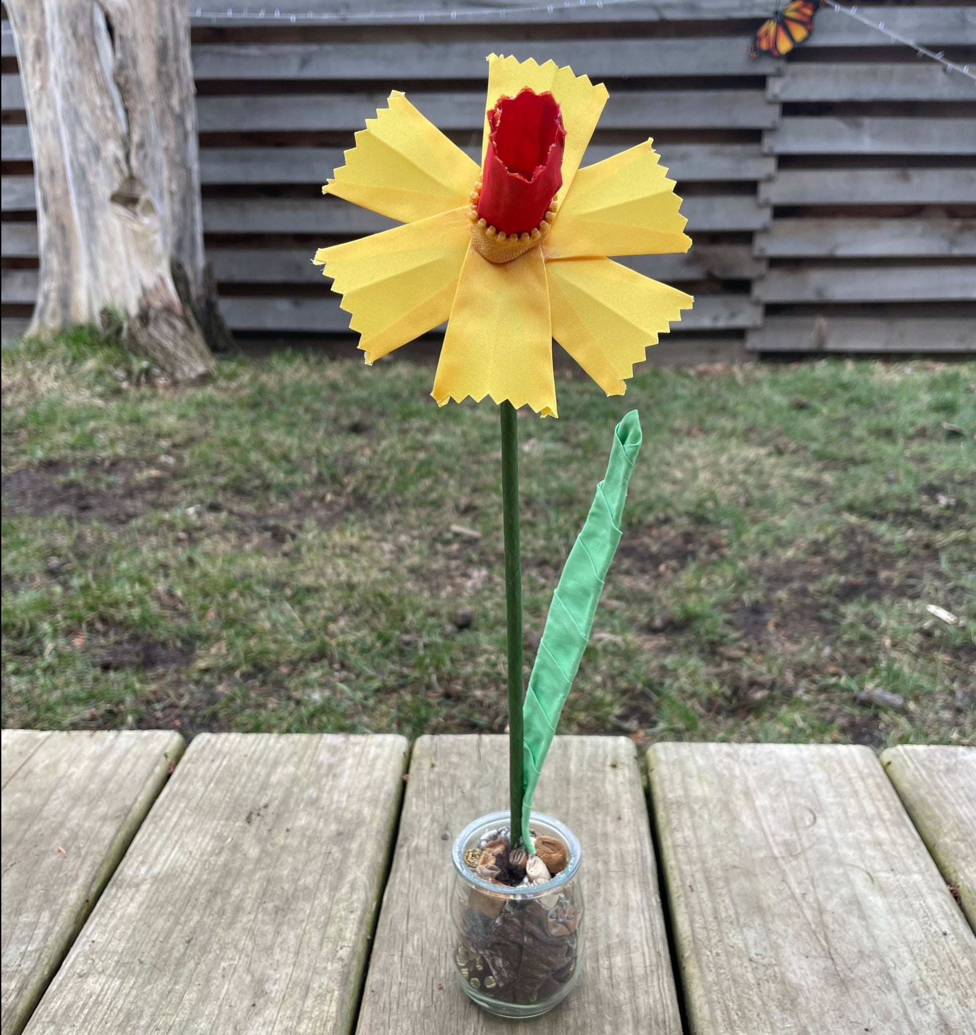 A daffodil made out of yellow ribbon sitting in a jar