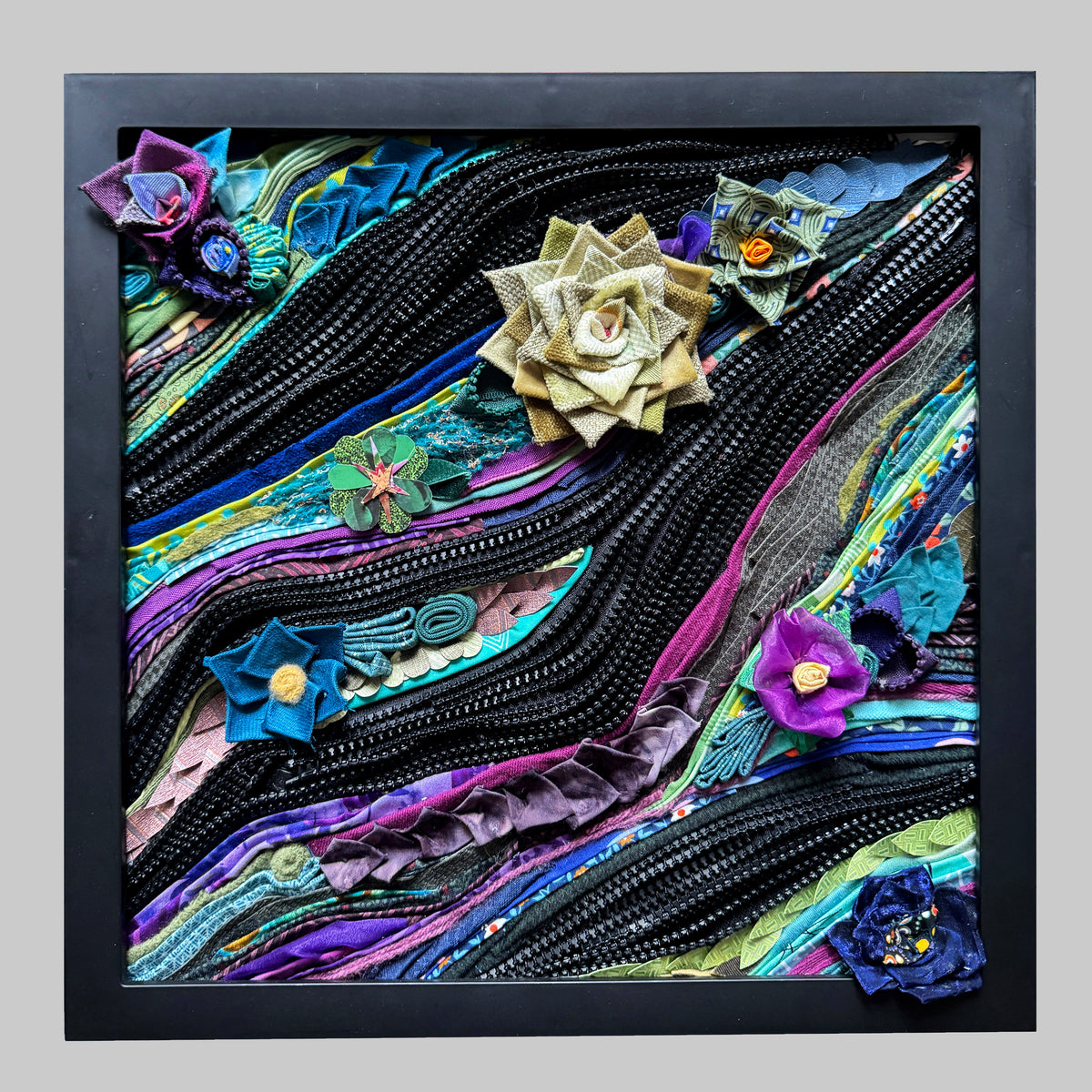 Colorful floral artwork made from fabric strips and zippers in a black frame.