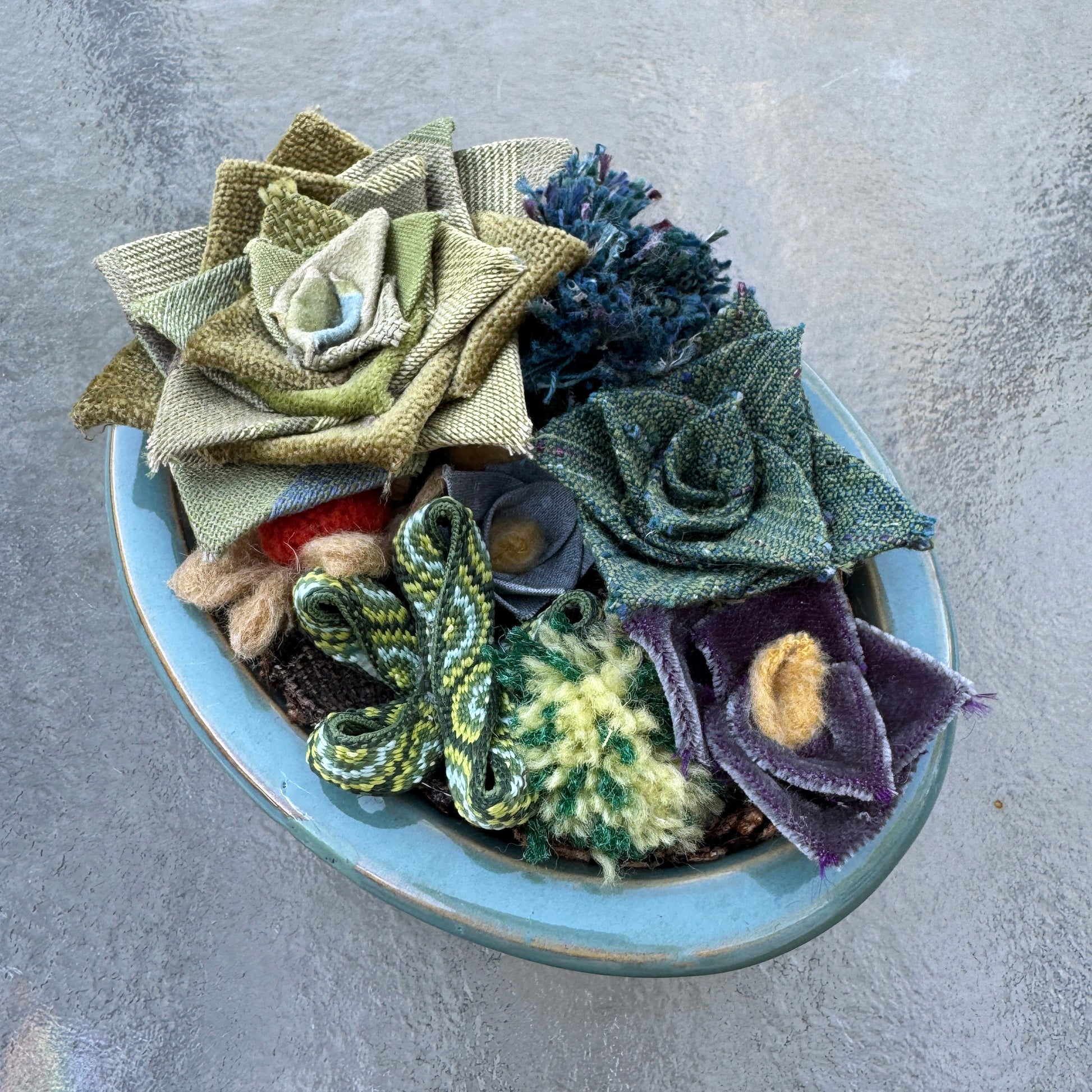 Collection of fabric and yarn succulents in a bowl on a textured glass surface