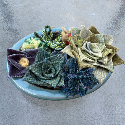 Collection of fabric flowers in a blue bowl on a gray surface
