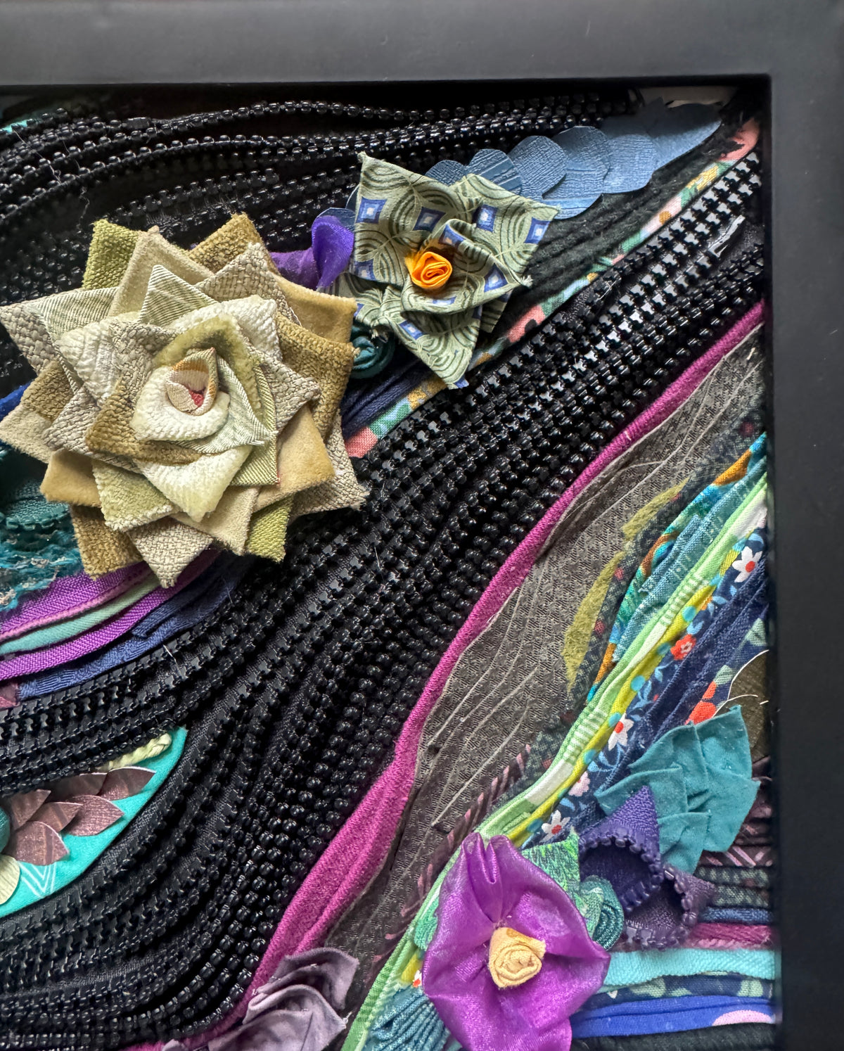 Colorful fabric art with floral patterns and textures in a black frame.