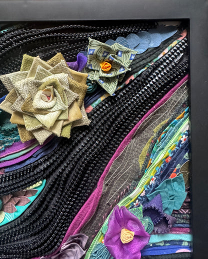 Colorful fabric art with floral patterns and textures in a black frame.